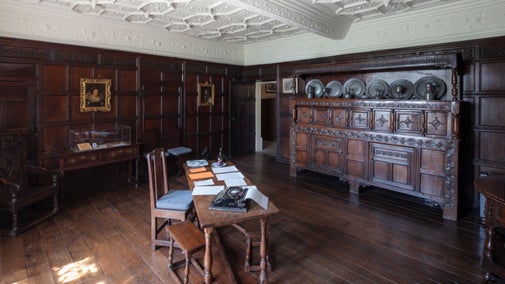 A dark panelled room with a white plaster ceiling and dark, period furniture.